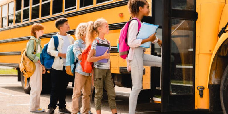Schoolchildren kids pupils group of mixed-race classmates boarding school bus before going to lessons, coming back to school, standing in line. New educational year semester.